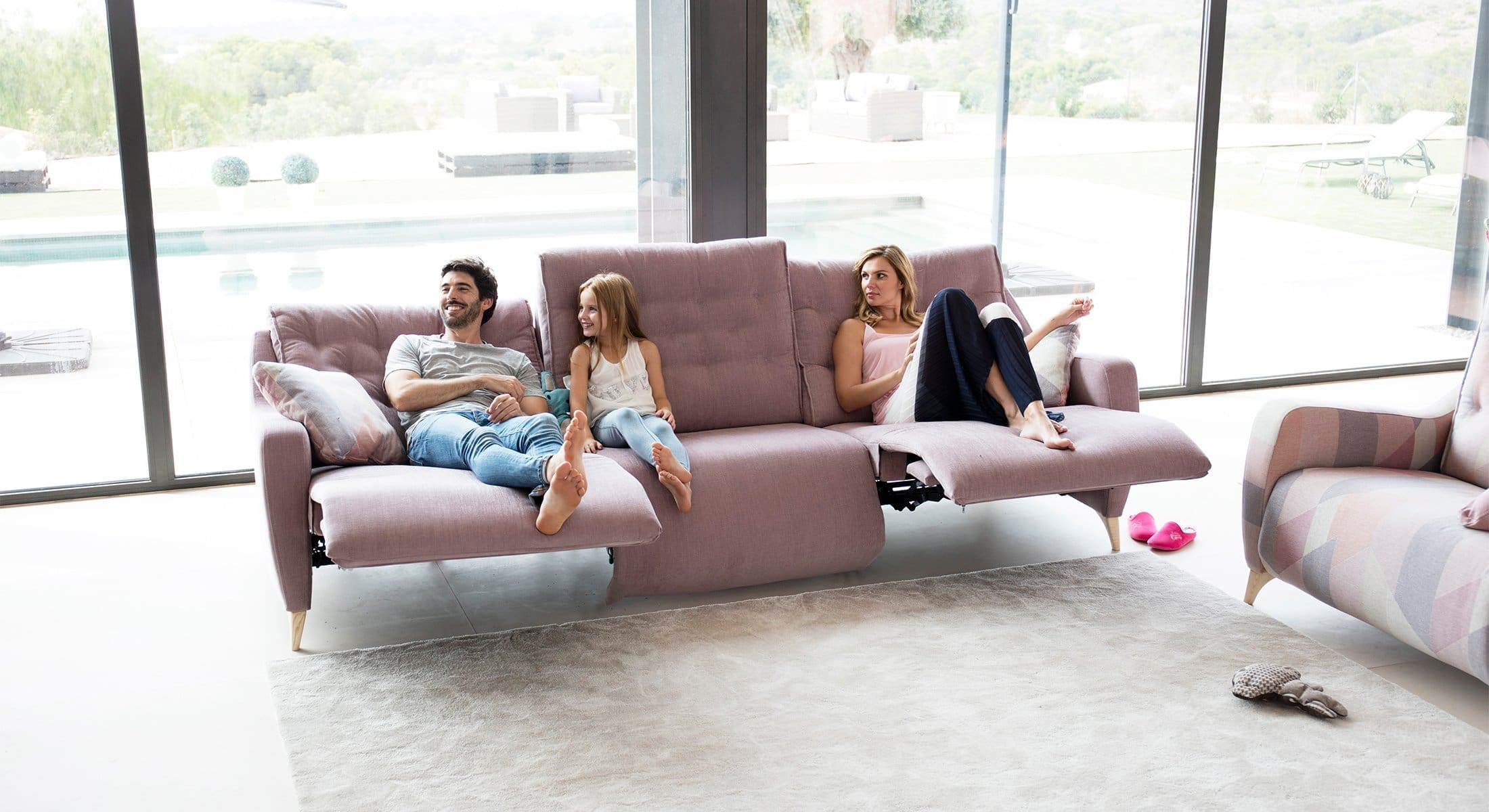 Relaxbank bij Houweling Interieur. Het is een bank met relaxfunctie uitgevoerd in lichtroze stof.