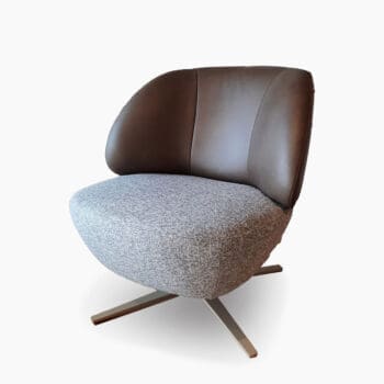 Moderne fauteuil bij Houweling Interieur. Het is een ronde fauteuil uitgevoerd in bruinleren rug en grijze stoffen zitting met spinpoot.