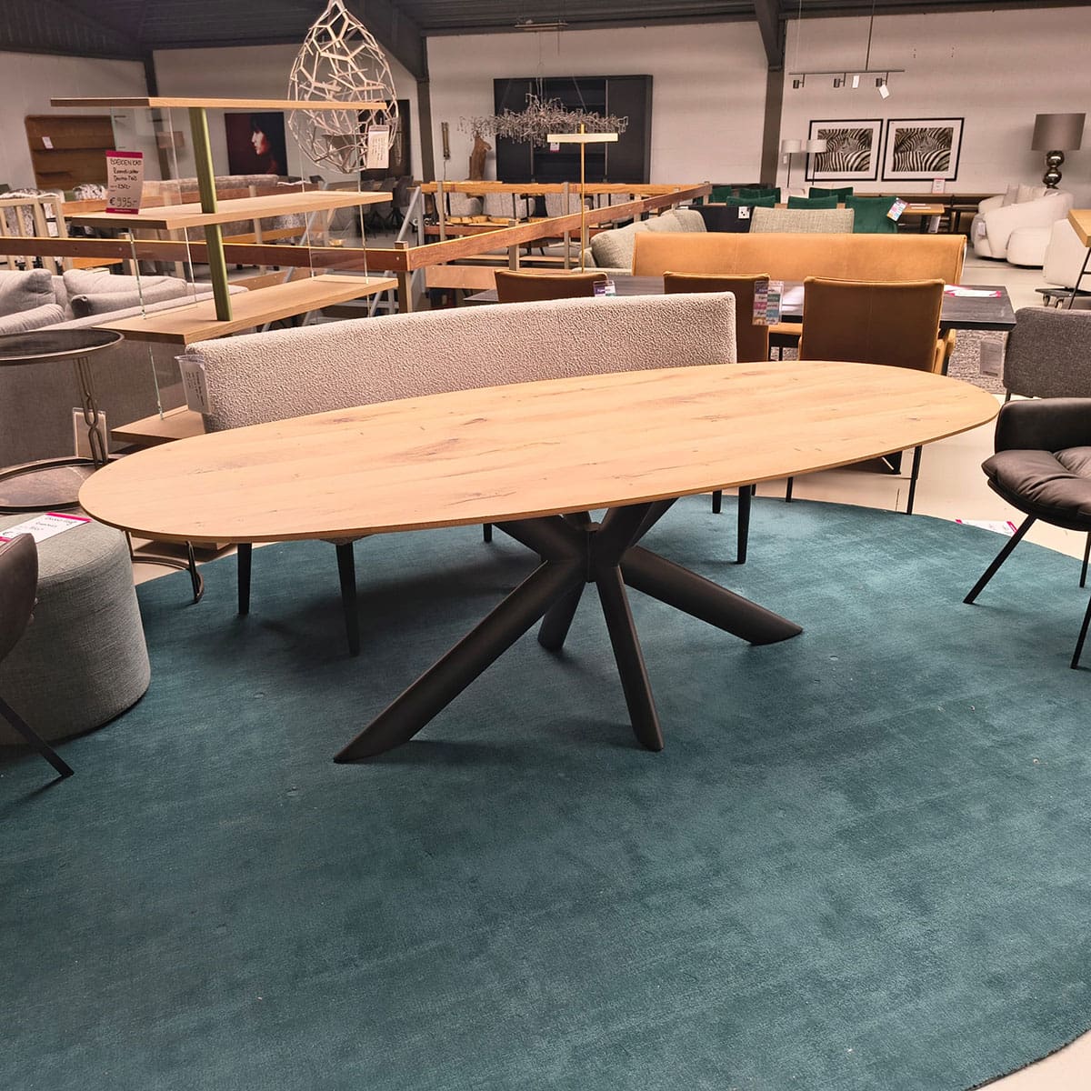 Showroommodel van een ovale eettafel bij Houweling Interieur. Houten eettafel uitgevoerd met bruinmetalen spinpoot.
