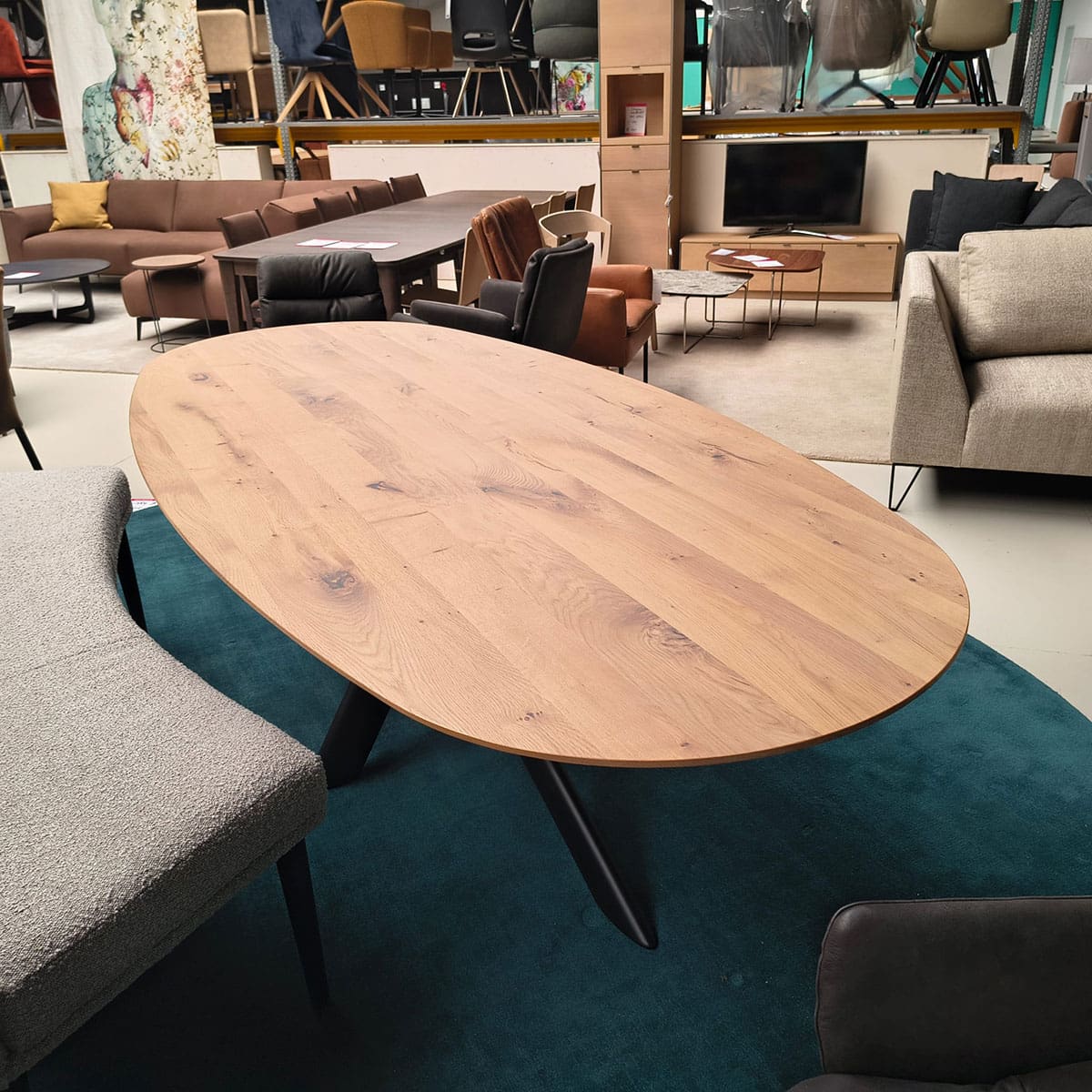 Showroommodel van een ovale eettafel bij Houweling Interieur. Houten eettafel uitgevoerd met bruinmetalen spinpoot.